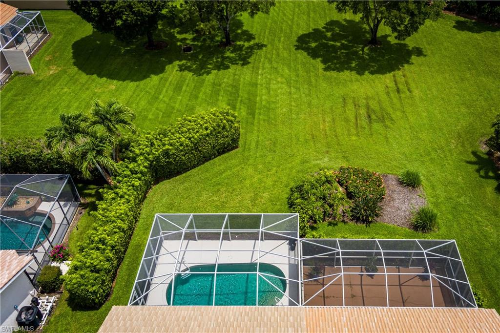 6658 Castlelawn Place, Unit 9 Naples, FL 34113 - Photo 32 of 38 Screened-in pool and patio area featuring a freeform swimming pool with a concrete deck, bordered by mature hedges