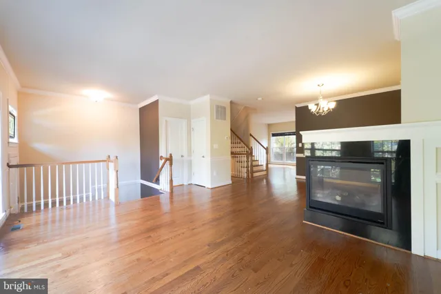 a view of an empty room with wooden floor fire place and a kitchen view