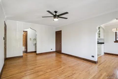 a view of an empty room with wooden floor and a ceiling fan