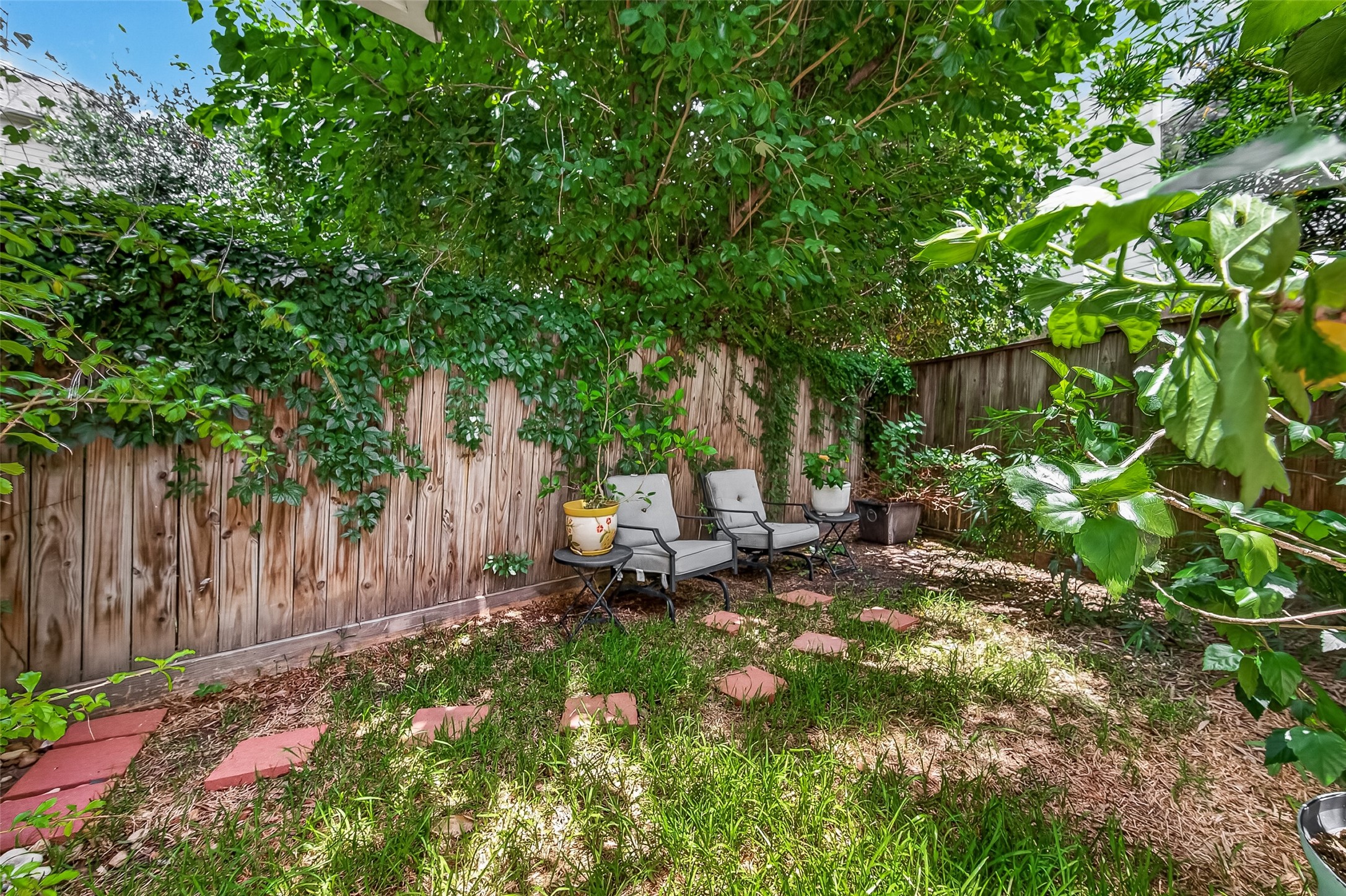 1767 Michigan Street Houston, TX 77006 - Photo 32 of 33 This cozy backyard features lush greenery, a wooden fence with climbing plants, and a small seating area, perfect for relaxation and outdoor enjoyment.