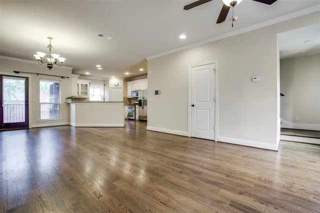 an empty room with chandelier fan and kitchen view