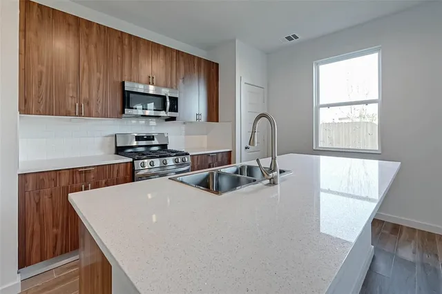 a kitchen with stainless steel appliances a sink a microwave a refrigerator and wooden cabinets