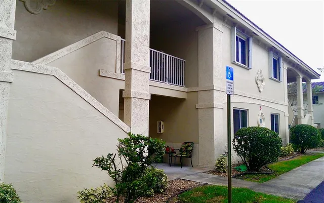 a view of white house with a small yard plants and large tree