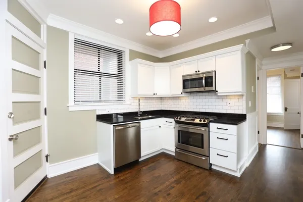 a kitchen with granite countertop a stove top oven a sink dishwasher and a microwave oven on the wooden floor