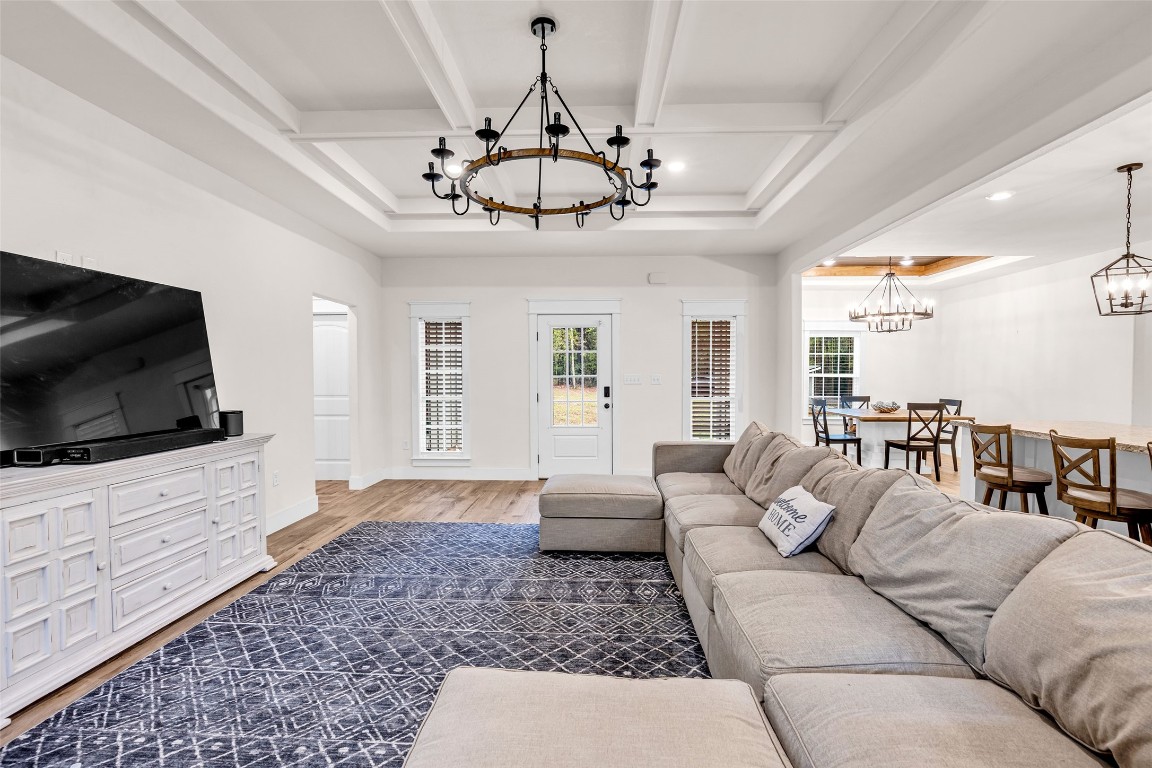 10040 Shepard Hill Road Willis, TX 77318 - Photo 12 of 36 This photo showcases a spacious and inviting living area with a large sectional sofa and a stylish chandelier. It features hardwood floors, a coffered ceiling, and an open layout flowing into a dining area with ample natural light. Ideal for comfortable living and entertaining.