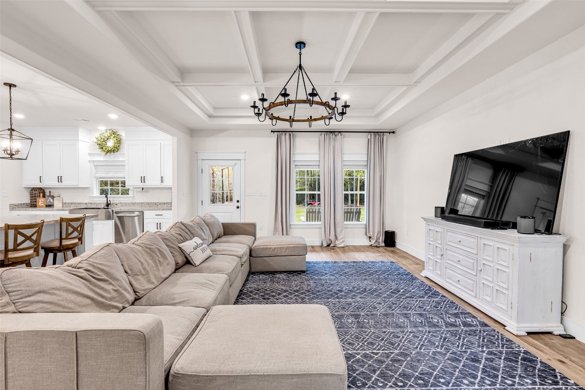 10040 Shepard Hill Road Willis, TX 77318 - Photo 13 of 36 This inviting living room features an open layout with a large sectional sofa, a stylish chandelier, and a substantial flat-screen TV on a white console. The space flows seamlessly into a modern kitchen with white cabinetry and a breakfast bar, all enhanced by natural light from large windows.