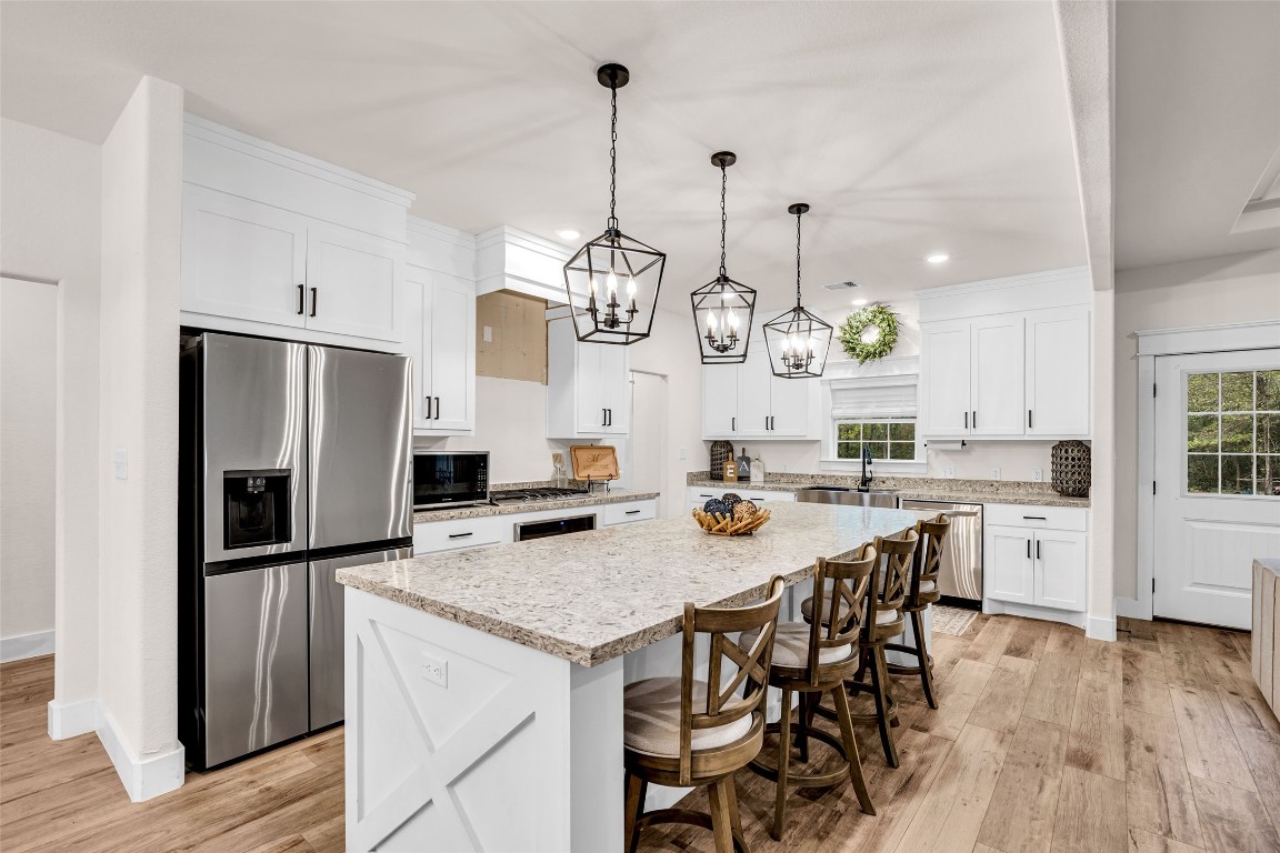 10040 Shepard Hill Road Willis, TX 77318 - Photo 17 of 36 This kitchen features a spacious layout with a large island and seating for four. It boasts modern stainless steel appliances, white cabinetry, and elegant pendant lighting. The wooden floor adds warmth, and there's ample natural light from the windows.