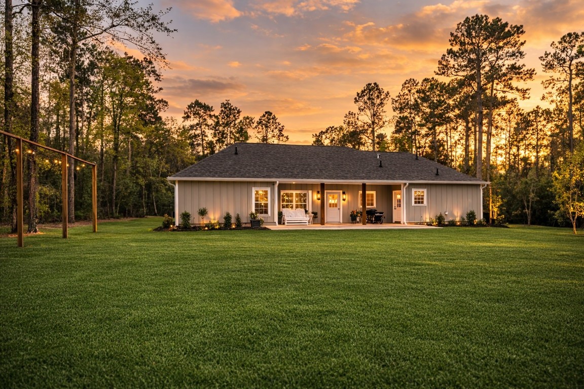 10040 Shepard Hill Road Willis, TX 77318 - Photo 2 of 36 This photo showcases a charming single-story home with a modern farmhouse style, set against a backdrop of tall trees. The spacious lawn and inviting porch create a warm and welcoming atmosphere, perfect for enjoying serene sunsets.