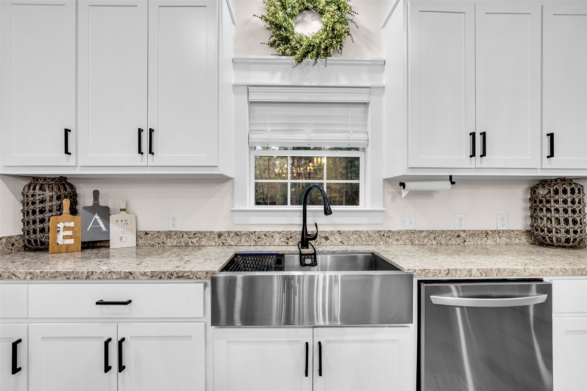 10040 Shepard Hill Road Willis, TX 77318 - Photo 22 of 36 This kitchen features modern white cabinetry with black handles, a sleek farmhouse sink, and stainless steel appliances. The granite countertops and decorative elements create a stylish and functional space.