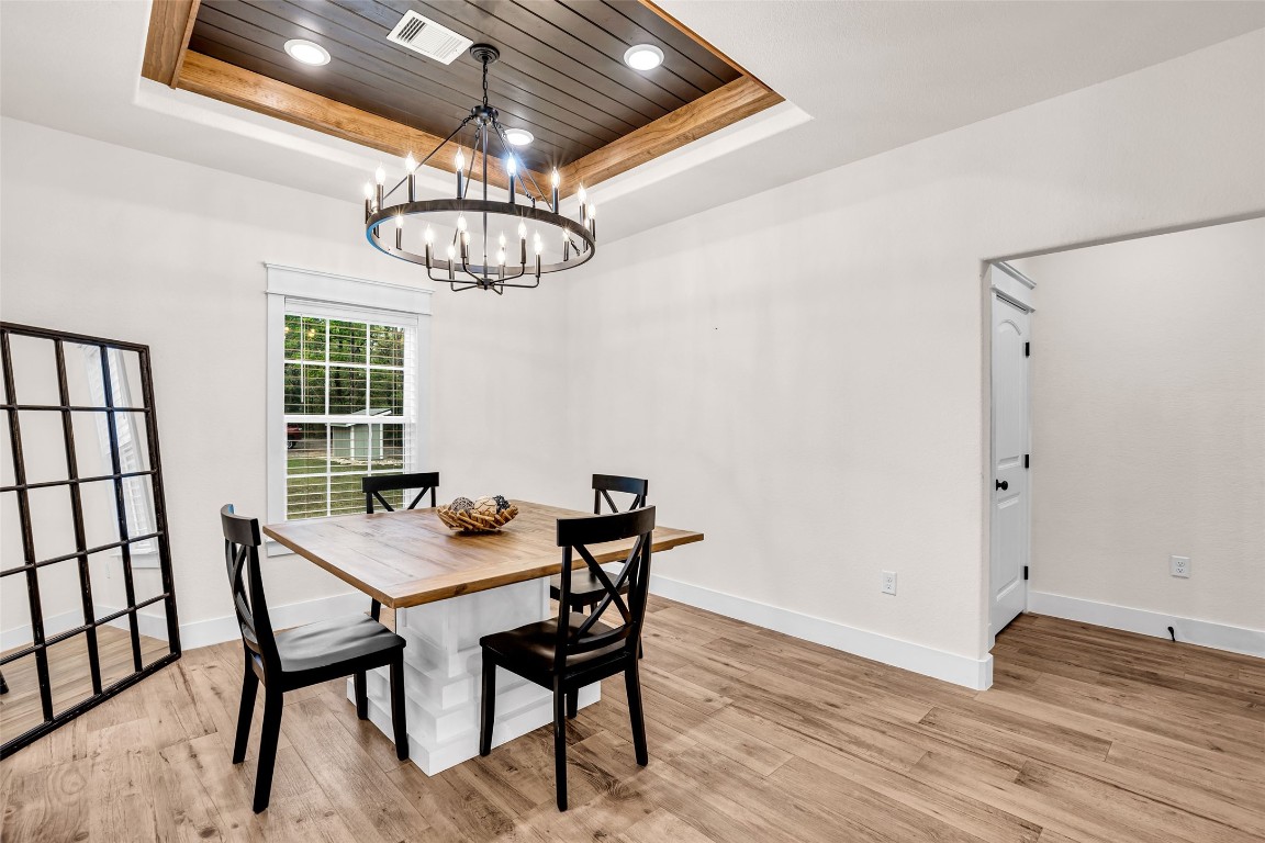 10040 Shepard Hill Road Willis, TX 77318 - Photo 25 of 36 This photo showcases a bright dining area with a modern chandelier, wood flooring, and a coffered ceiling. It features a large window for natural light, a wooden table with black chairs, and an adjacent doorway for easy access.