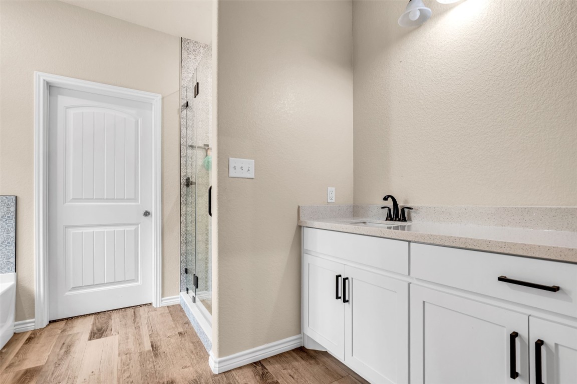 10040 Shepard Hill Road Willis, TX 77318 - Photo 29 of 36 This bathroom features a sleek modern design with a spacious vanity, white cabinetry, and black fixtures. It includes a glass-enclosed shower and a wooden floor, creating a clean and inviting space.