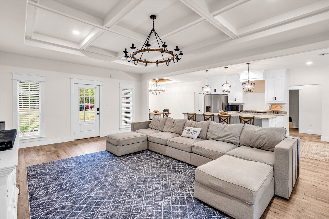 10040 Shepard Hill Road Willis, TX 77318 - Photo 3 of 36 This inviting open-concept living area features a spacious sectional, elegant coffered ceiling with a chandelier, and a modern kitchen with a large island and bar seating, all complemented by warm wood flooring and abundant natural light.