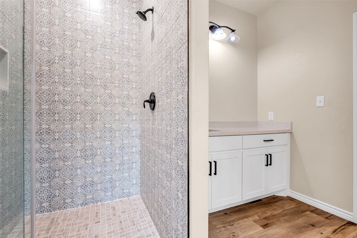 10040 Shepard Hill Road Willis, TX 77318 - Photo 31 of 36 This bathroom features a stylish walk-in shower with intricate patterned tiles and a glass door. Adjacent is a vanity area with a light-colored countertop and white cabinetry, complemented by wood flooring.