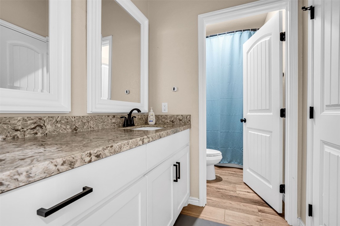 10040 Shepard Hill Road Willis, TX 77318 - Photo 33 of 36 This bathroom features a spacious vanity with a marble-look countertop, dual mirrors, and sleek black fixtures. The room includes a private toilet area with a blue shower curtain, set against warm beige walls and light wood-look flooring for a modern, clean aesthetic.