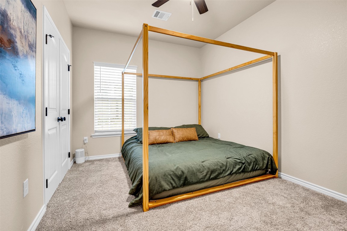 10040 Shepard Hill Road Willis, TX 77318 - Photo 34 of 36 This bedroom features a cozy carpeted floor, a modern four-poster bed with green bedding, and natural light from a window with blinds. Neutral walls and a ceiling fan complete the space, offering a comfortable retreat.