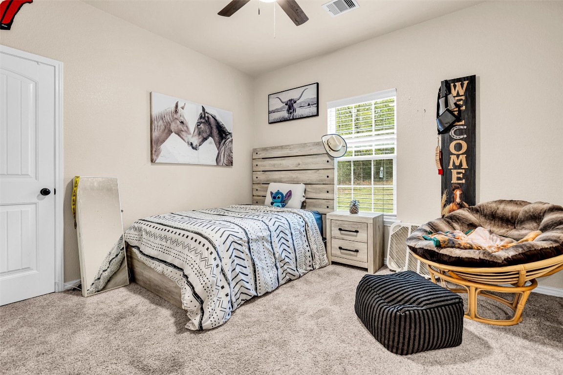 10040 Shepard Hill Road Willis, TX 77318 - Photo 35 of 36 Cozy bedroom with neutral tones, featuring a single bed, a rustic wooden headboard, and a bedside table. Decor includes animal-themed wall art, a welcome sign, and a comfortable papasan chair. Carpeted floors and a window providing natural light complete the space.