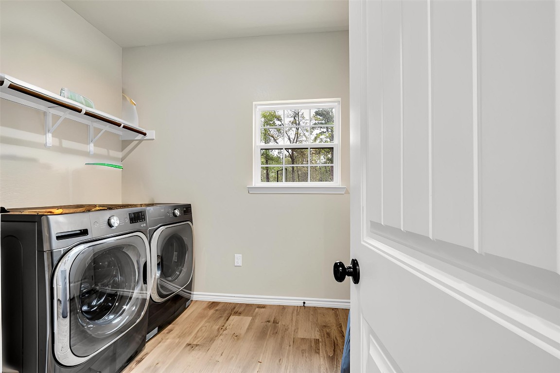 10040 Shepard Hill Road Willis, TX 77318 - Photo 36 of 36 This photo features a bright laundry room with modern appliances, light wood flooring, and a small window providing natural light. Shelving above the machines offers additional storage.