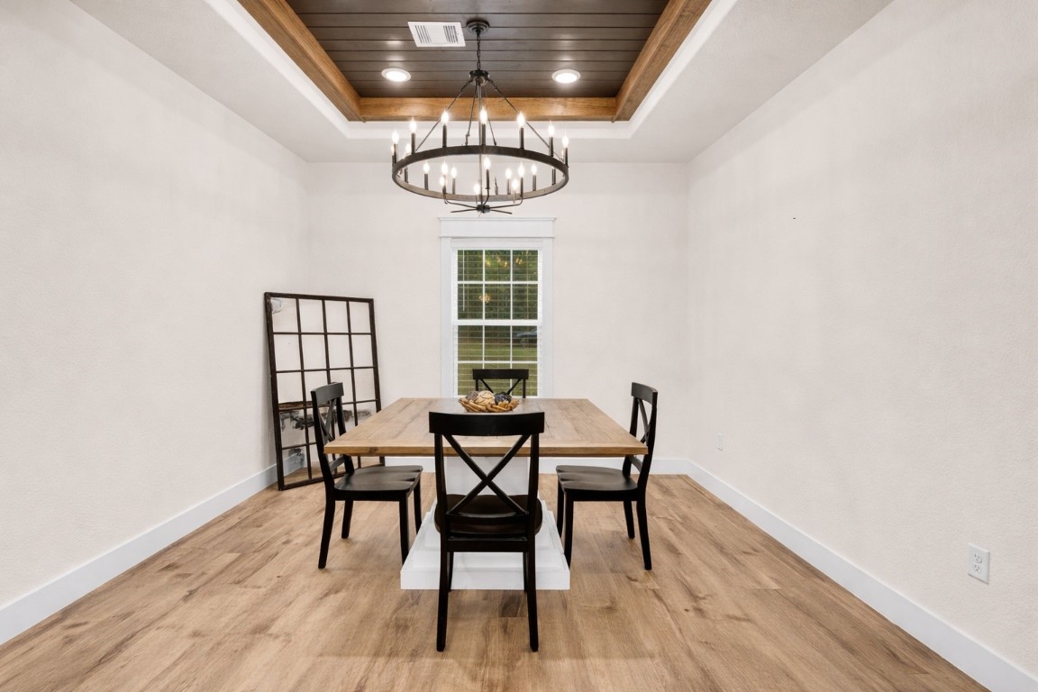 10040 Shepard Hill Road Willis, TX 77318 - Photo 4 of 36 This dining room features a modern, minimalist design with a wooden table and four chairs. A stylish chandelier hangs from a recessed ceiling with wood accents. Light wood flooring complements the bright, airy atmosphere, enhanced by a large window and decorative mirror.