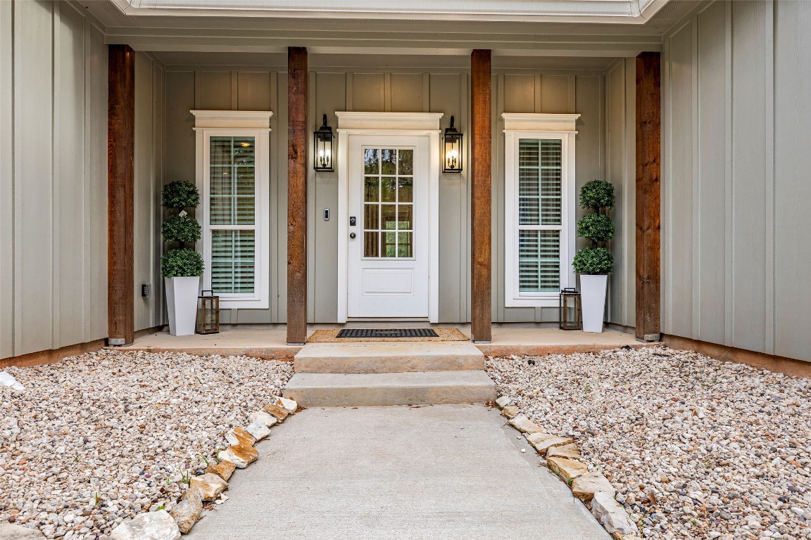 10040 Shepard Hill Road Willis, TX 77318 - Photo 6 of 36 This inviting home features a charming front entrance with a white door flanked by tall windows. Rustic wooden columns enhance the modern look, complemented by neatly arranged potted plants and stylish wall lanterns. A stone path adds natural appeal, leading to a welcoming porch.