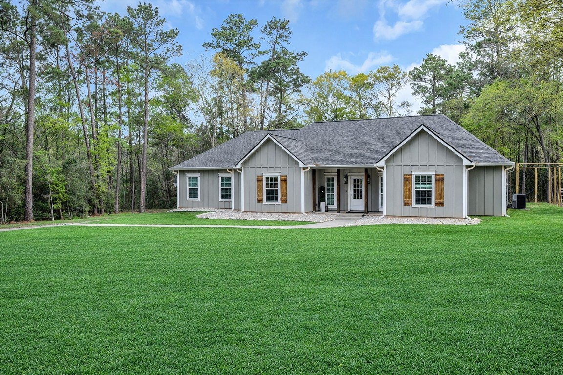 10040 Shepard Hill Road Willis, TX 77318 - Photo 7 of 36 Charming single-story home with a gray exterior and wood shutter accents, set in a lush green lawn surrounded by mature trees for added privacy. Features a welcoming front porch and a peaceful, natural setting.