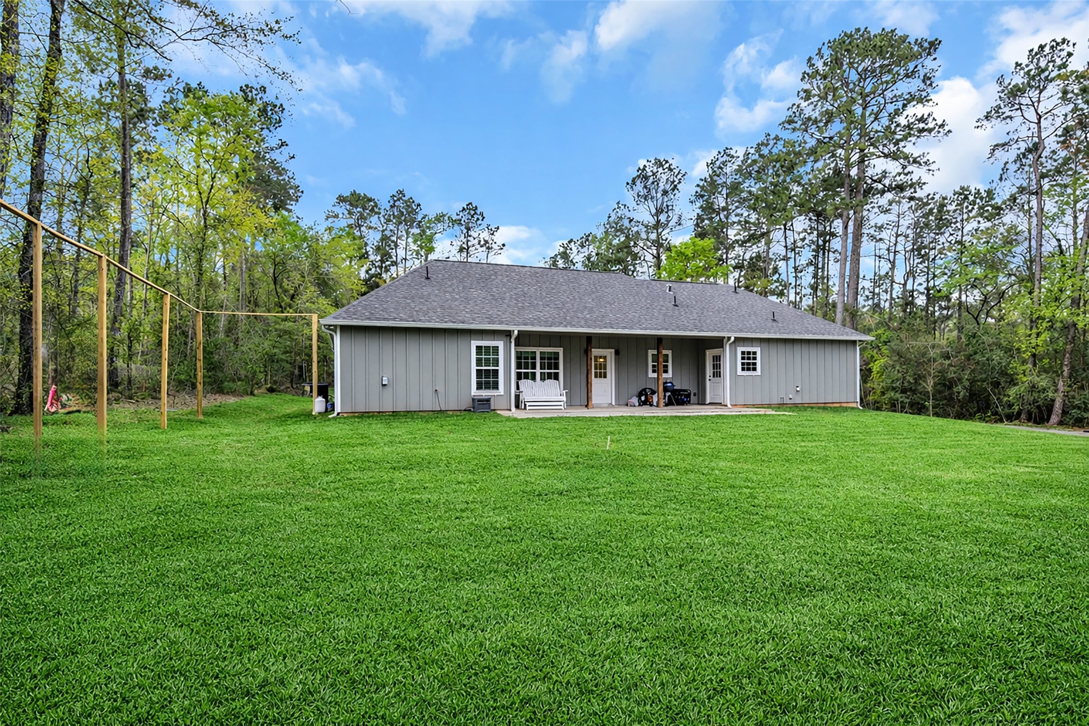 10040 Shepard Hill Road Willis, TX 77318 - Photo 8 of 36 This photo showcases a charming single-story gray home with a spacious, well-maintained backyard, surrounded by trees for added privacy. The house features a covered patio, perfect for outdoor relaxation or entertaining.