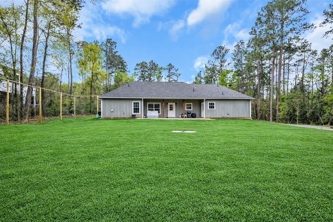 10040 Shepard Hill Road Willis, TX 77318 - Photo 9 of 36 This photo showcases the back of a charming single-story house with a spacious, well-maintained lawn surrounded by tall trees, offering a serene and private outdoor space.