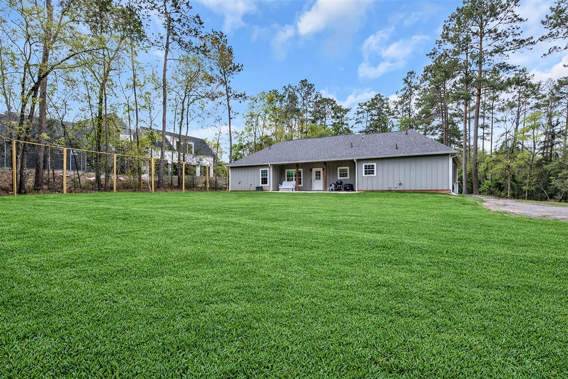 10040 Shepard Hill Road Willis, TX 77318 - Photo 10 of 36 This photo showcases a single-story home with a spacious and well-maintained backyard, bordered by tall trees, offering privacy and a serene environment. The house features a simple, modern exterior with a covered patio area. Ideal for those seeking a tranquil setting with ample outdoor space.