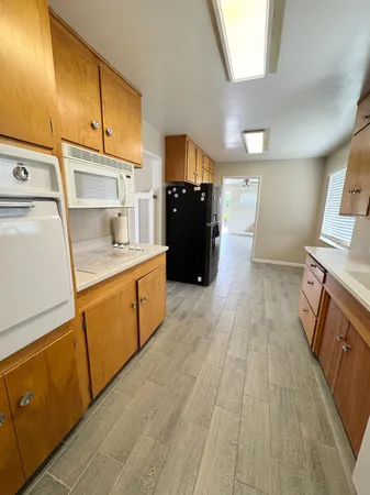a view of a refrigerator in kitchen and an empty room with wooden floor
