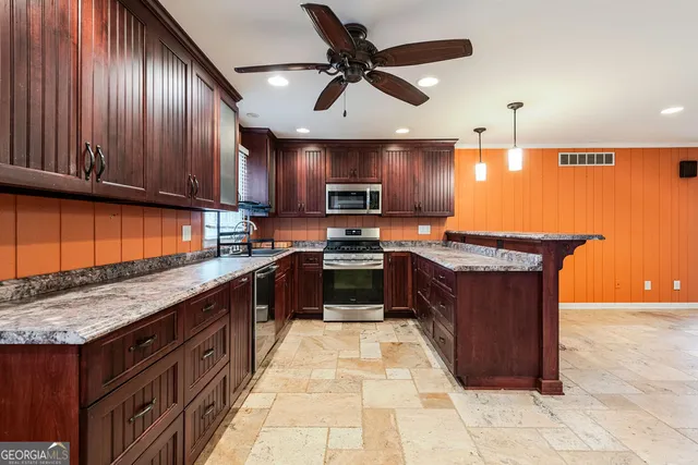 a kitchen with stainless steel appliances granite countertop wooden cabinets a sink a stove and a wooden floors