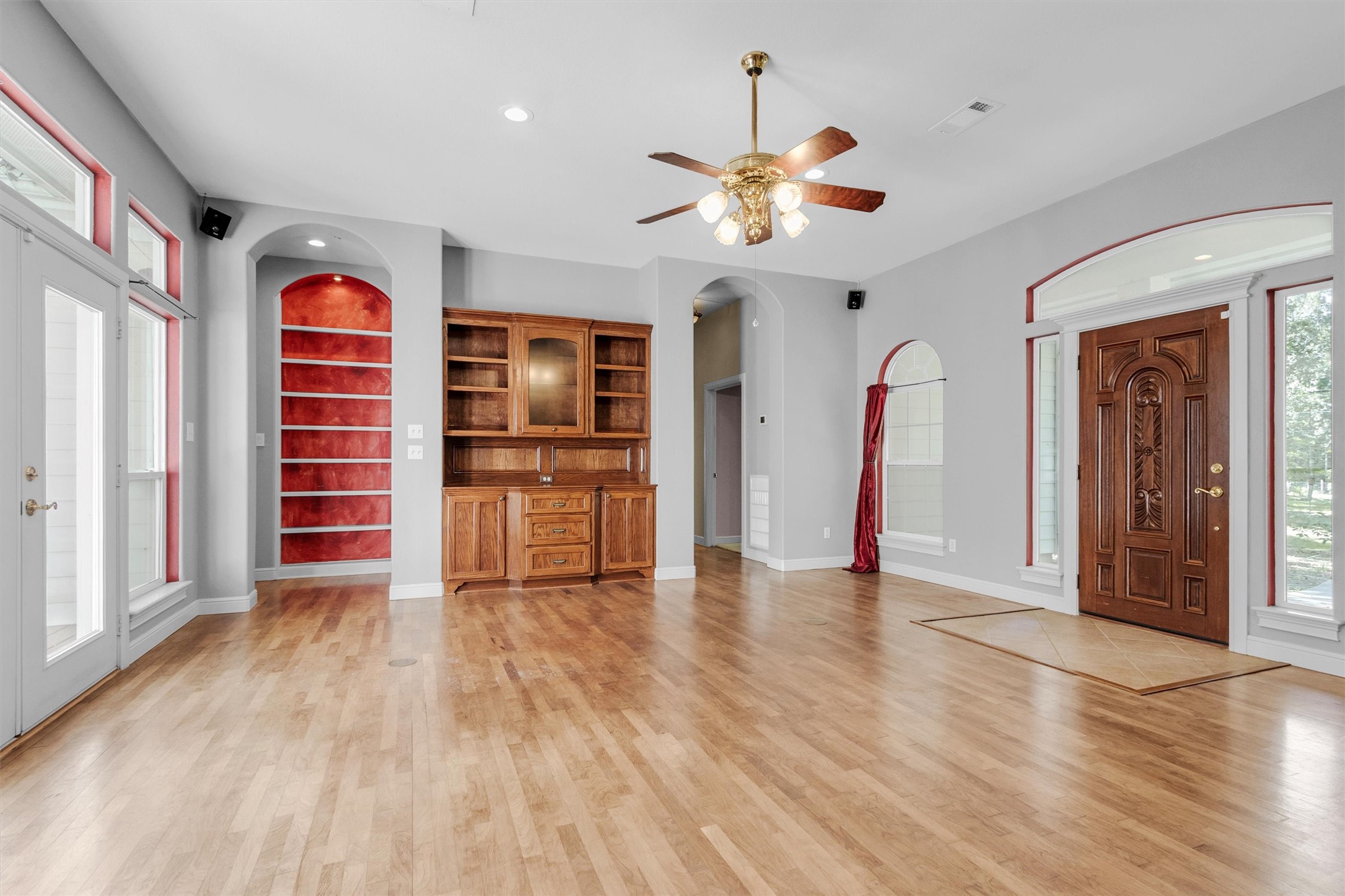 10331 Iron Ore Road Conroe, TX 77303 - Photo 6 of 47 Spacious living area with elegant hardwood floors, a stunning wooden built-in, and abundant natural light from large windows. The room features a decorative ceiling fan and an inviting wooden front door, creating a warm and welcoming atmosphere.