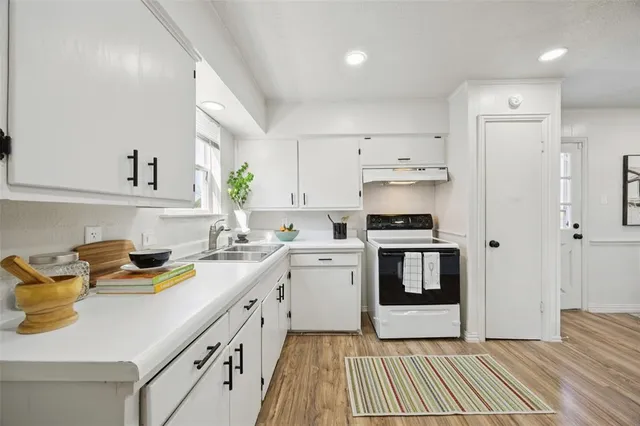 a kitchen with a sink dishwasher stove and white cabinets with wooden floor