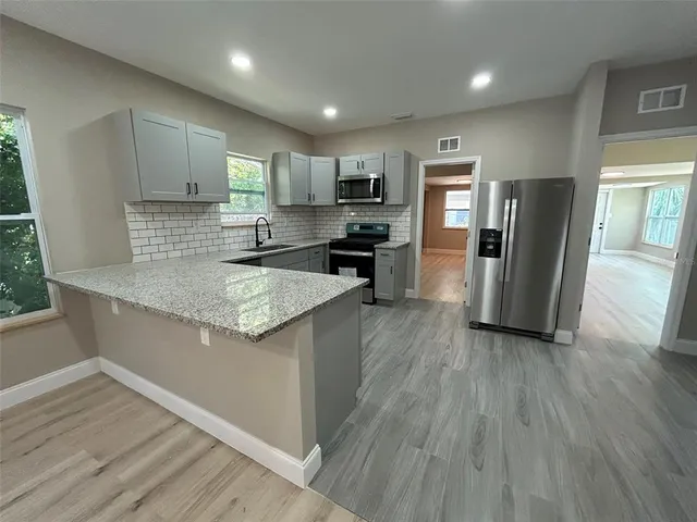 a kitchen with stainless steel appliances granite countertop a refrigerator a sink dishwasher a stove and white countertops with wooden floor