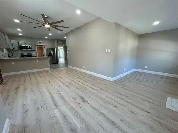 a view of an empty room with wooden floor and a kitchen
