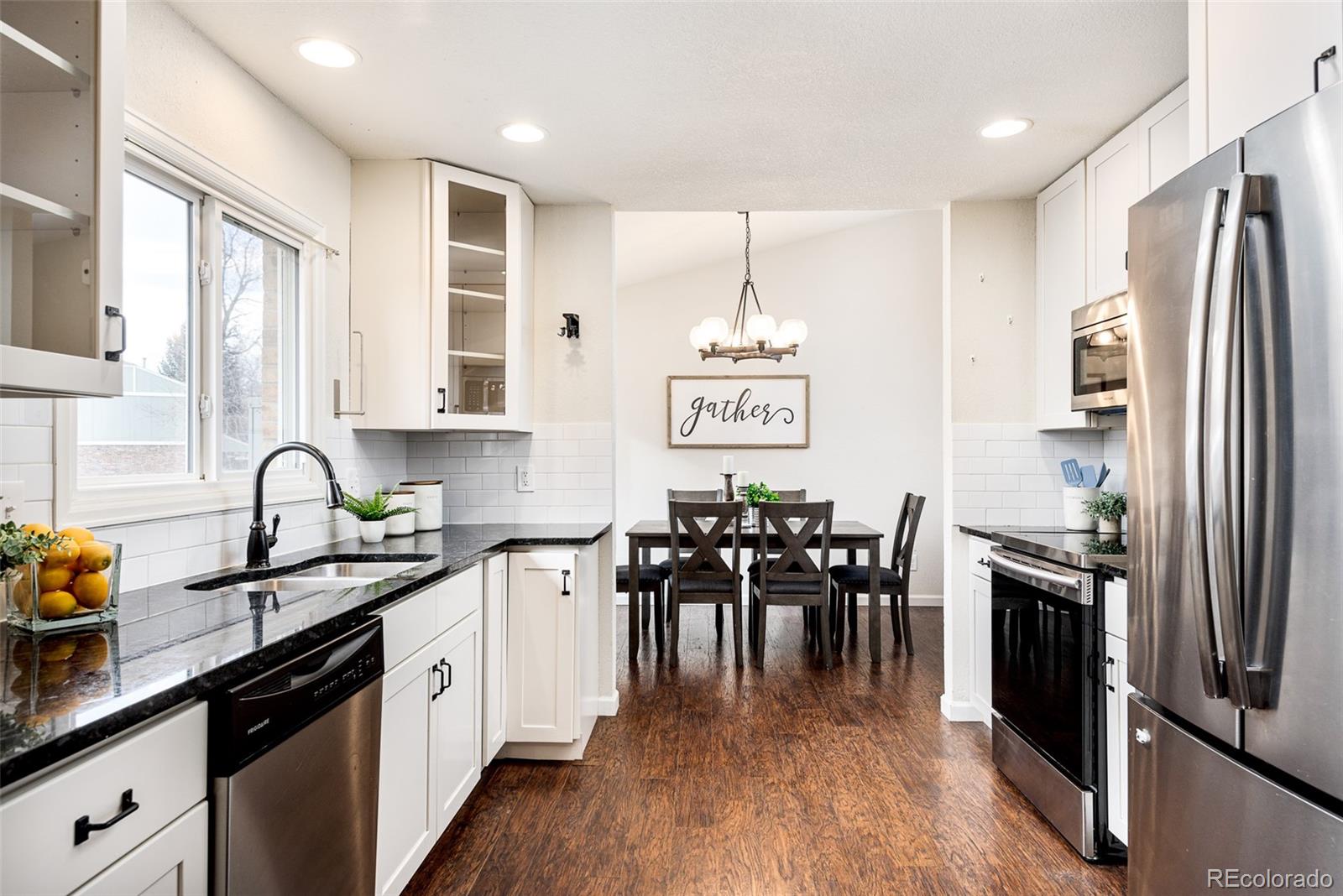 13492 Jackson Drive Thornton, CO 80241 - Photo 7 of 25 a kitchen with stainless steel appliances granite countertop a refrigerator a stove top oven a sink dishwasher a dining table and chairs with wooden floor