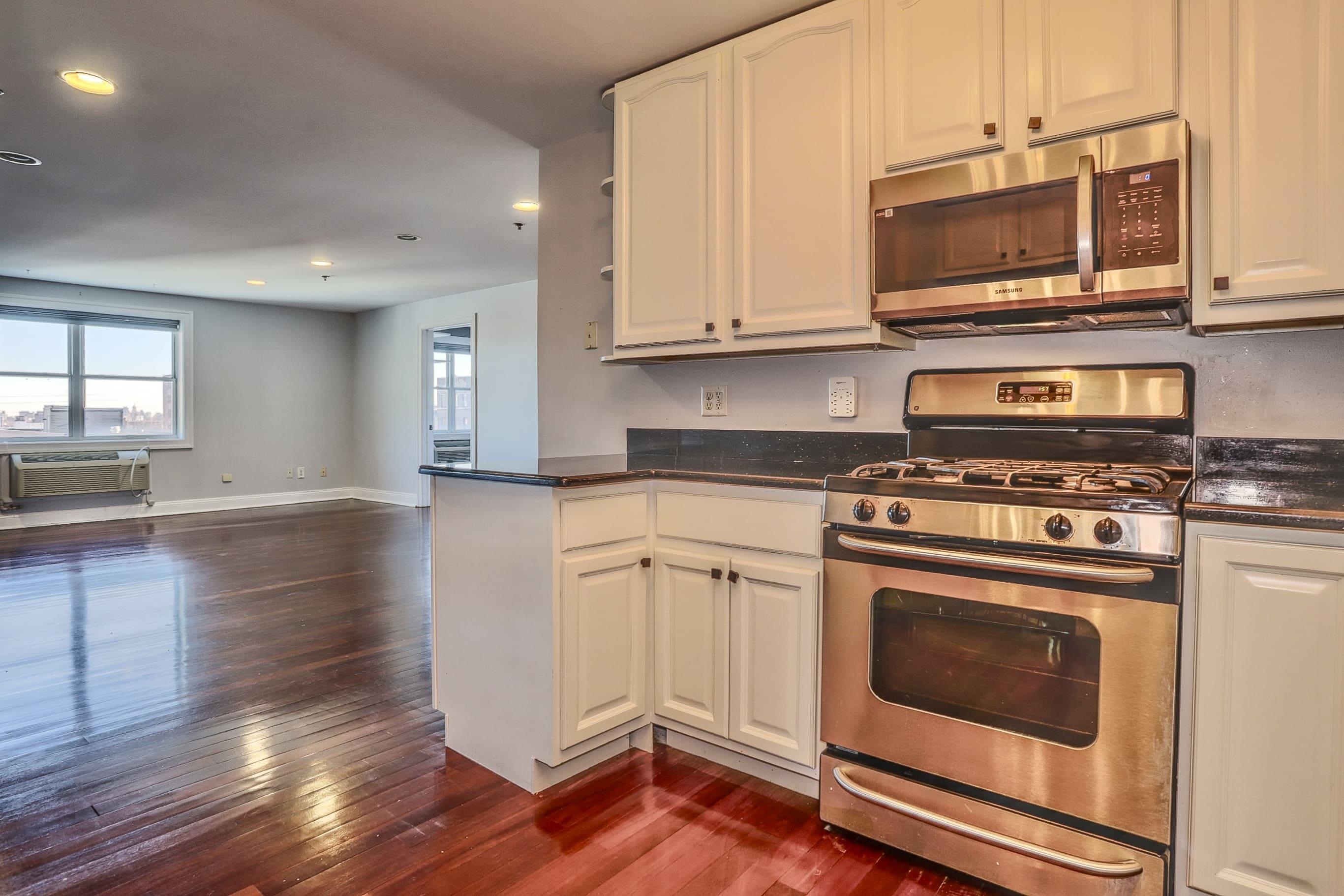 1720 New York Avenue, Unit 406 Union City, NJ 07087 - Photo 11 of 21 a kitchen with granite countertop a stove top oven a sink dishwasher and white cabinets with wooden floor