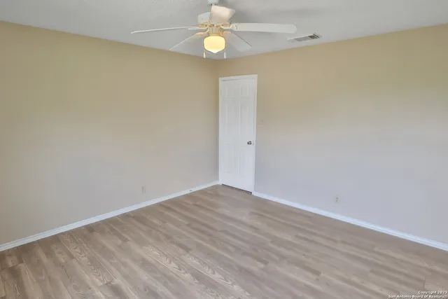 a view of an empty room with wooden floor and fan