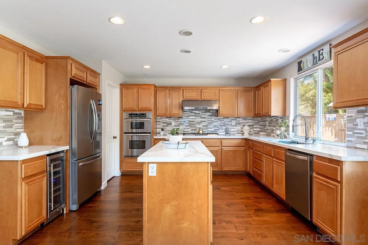 304 River Ranch Way Oceanside, CA 92057 - Photo 6 of 44 a large kitchen with stainless steel appliances granite countertop a refrigerator a sink dishwasher a stove top oven a large island with wooden cabinets and floor