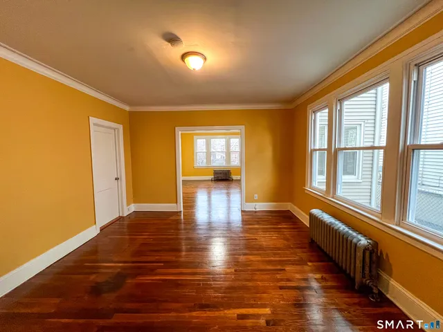 a view of an empty room with wooden floor and a window