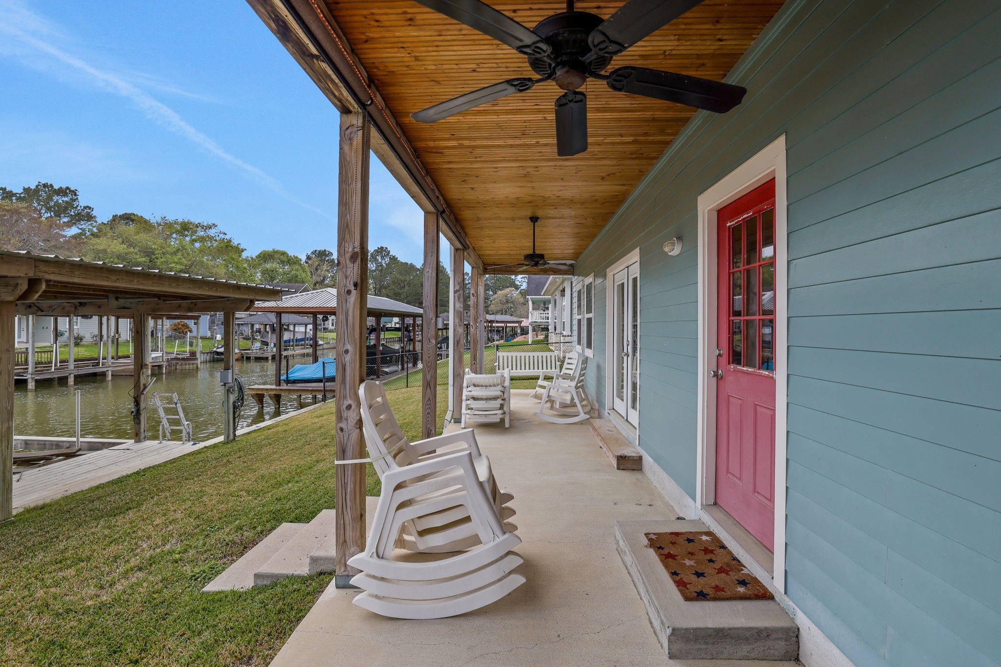 331 Holiday Lane Coldspring, TX 77331 - Photo 15 of 36 This photo showcases a waterfront porch with a wooden ceiling, ceiling fans, , perfect for relaxing. The porch overlooks a canal with boat docks, providing a serene and inviting outdoor space.