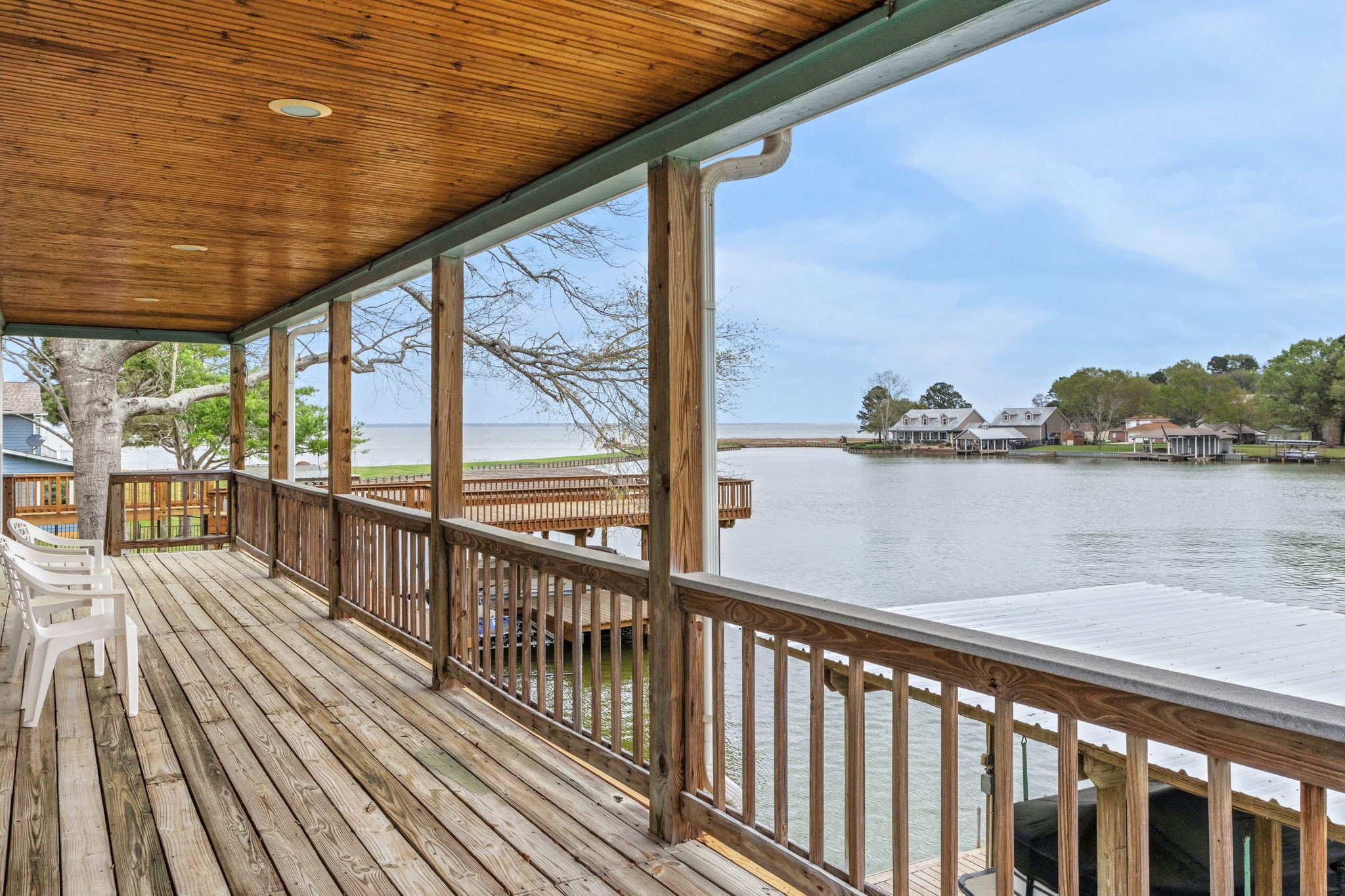 331 Holiday Lane Coldspring, TX 77331 - Photo 21 of 36 This photo showcases a spacious covered deck with wooden flooring and railing, offering a scenic view of a serene waterfront. Ideal for relaxation, and overlooks neighboring homes along the shore.