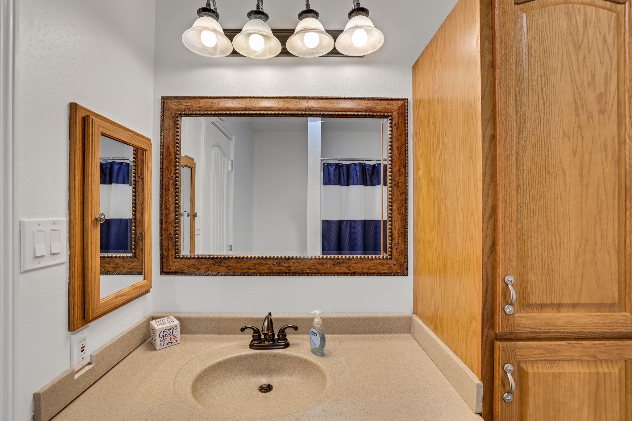 331 Holiday Lane Coldspring, TX 77331 - Photo 22 of 36 This bathroom features a stylish vanity with a granite countertop, an elegant framed mirror, and ample wooden cabinet storage. The lighting fixture above adds a classic touch, complementing the overall warm and inviting ambiance.