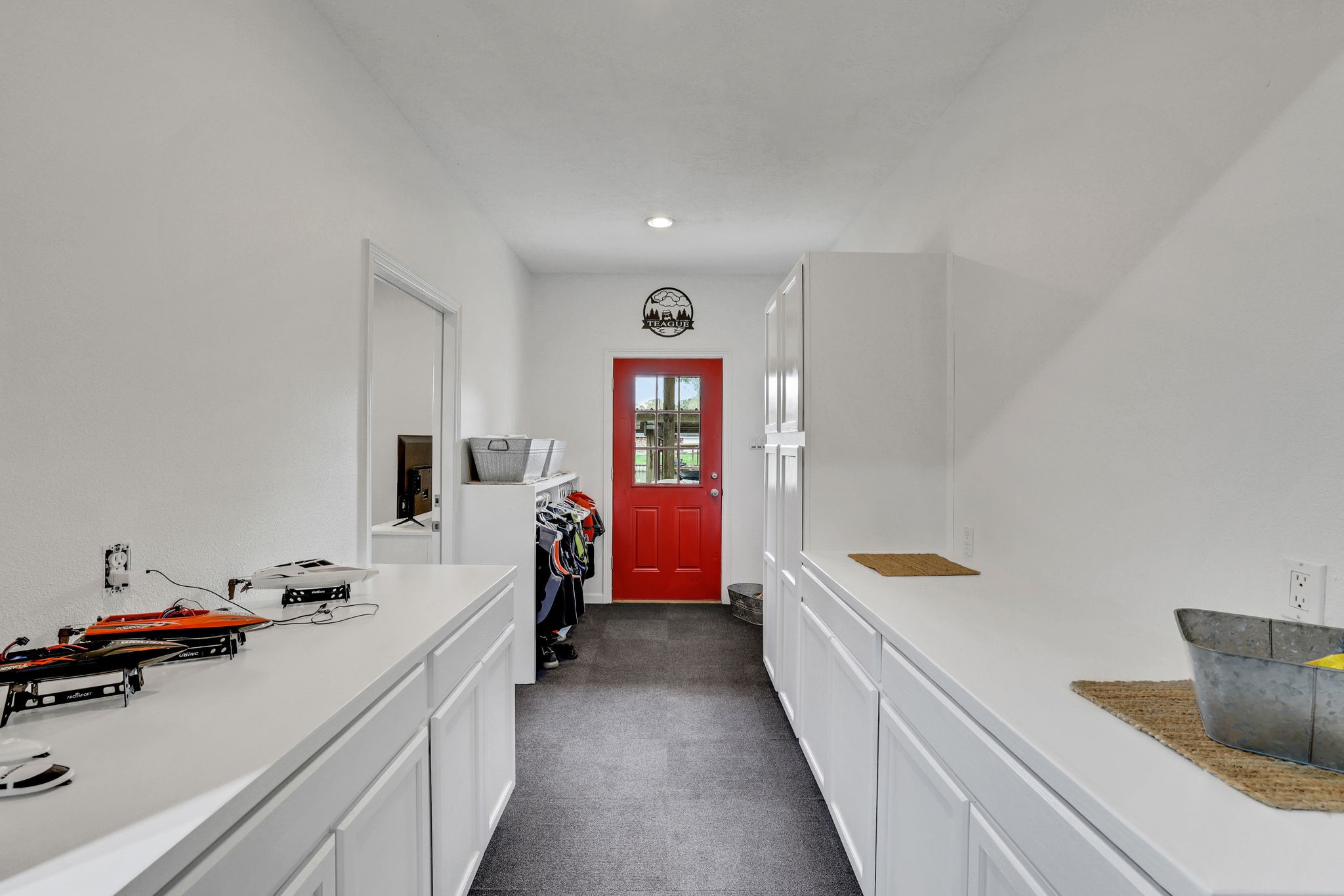 331 Holiday Lane Coldspring, TX 77331 - Photo 23 of 36 This photo shows a bright, spacious galley or mudroom with white cabinetry, a countertop, and a bold red door. The room is well-lit with recessed lighting, offering ample storage and workspace.