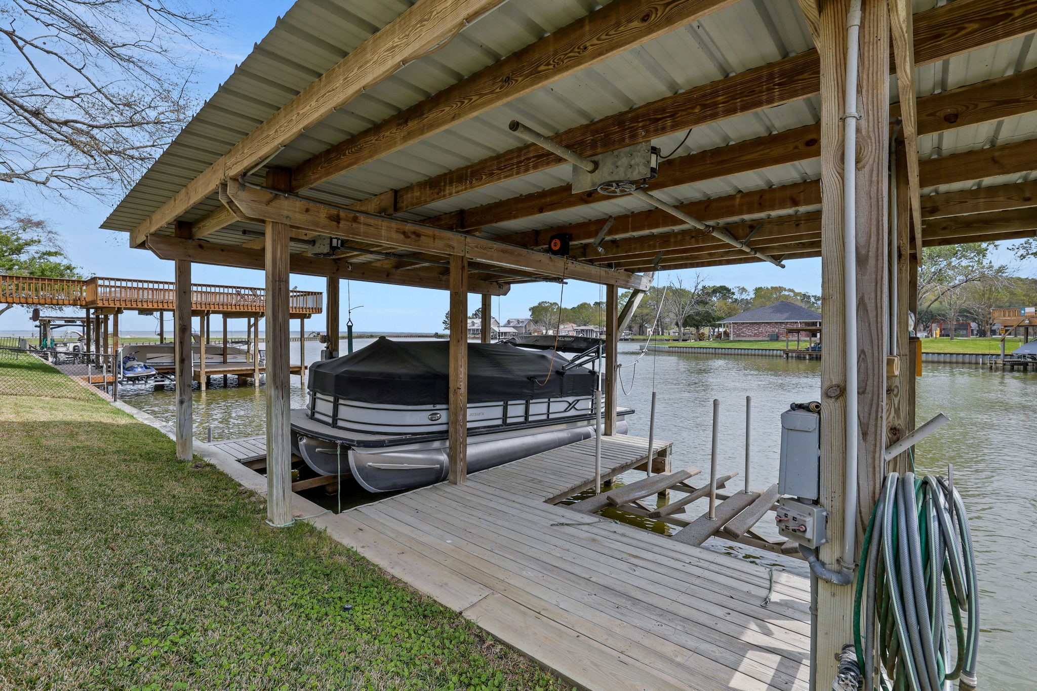 331 Holiday Lane Coldspring, TX 77331 - Photo 28 of 36 This photo showcases a covered boat dock with a lift on a serene waterfront property. It features a well-maintained wooden structure, ample space for boat storage, and scenic water views, perfect for boating enthusiasts.
