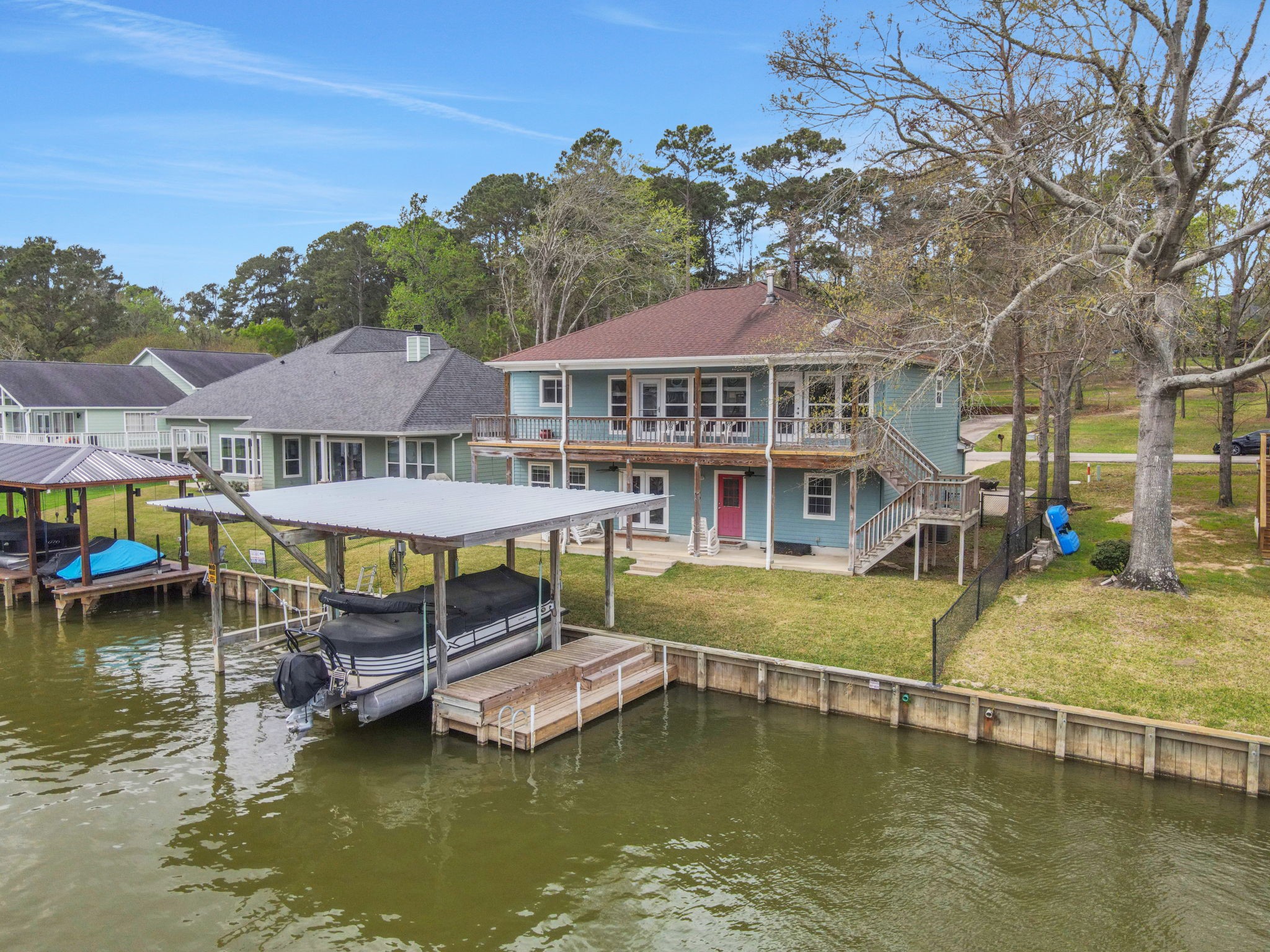 331 Holiday Lane Coldspring, TX 77331 - Photo 3 of 36 This waterfront home features a two-story design with a spacious balcony overlooking the lake and a fenced backyard. It has direct access to a covered boat dock, perfect for boating enthusiasts. The property is surrounded by lush greenery and offers a serene, scenic setting.