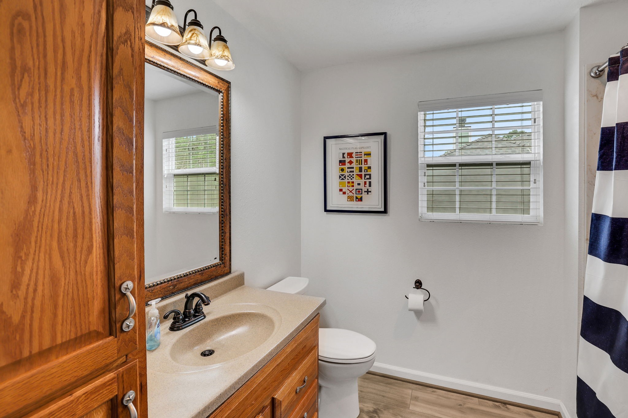 331 Holiday Lane Coldspring, TX 77331 - Photo 31 of 36 This bathroom features a wooden vanity with a large mirror, modern light fixtures, and a neutral countertop. It includes a window for natural light.