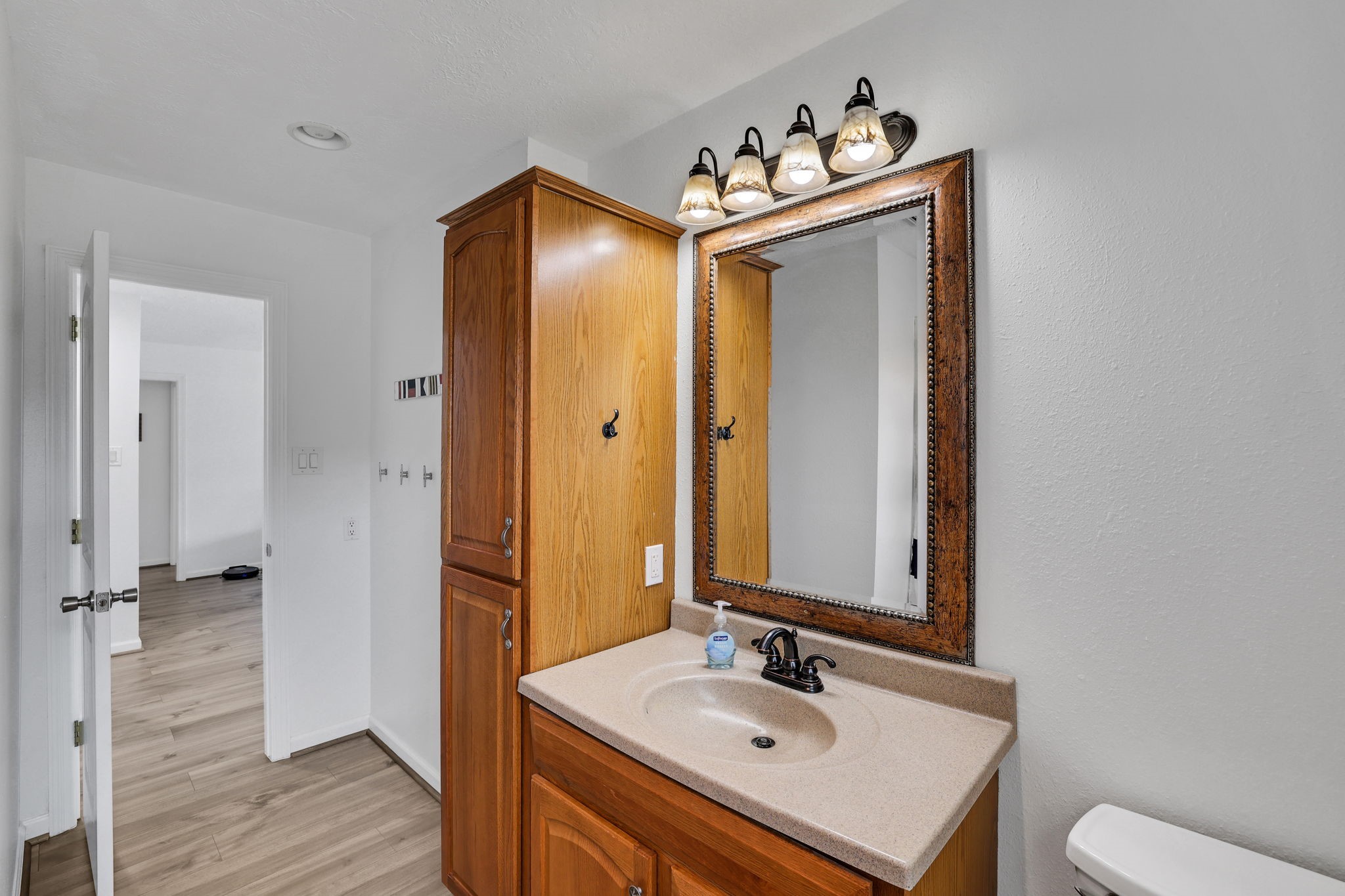 331 Holiday Lane Coldspring, TX 77331 - Photo 32 of 36 This bathroom features a wooden vanity with ample storage, a large framed mirror, and elegant lighting. It opens to a bright hallway with warm wood flooring.