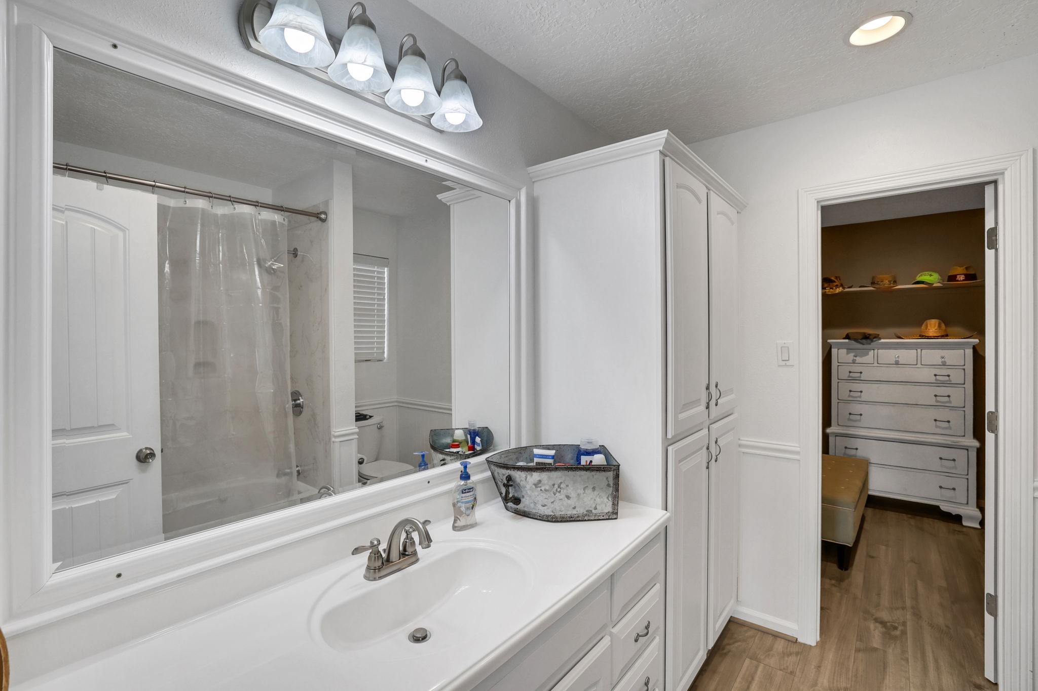 331 Holiday Lane Coldspring, TX 77331 - Photo 34 of 36 This primary bathroom features a clean, modern design with white cabinetry and ample storage. It includes a large mirror, a sink with a sleek faucet, and a shower with a glass door. The space is bright with overhead lighting and connects to a walk-in closet with additional storage.