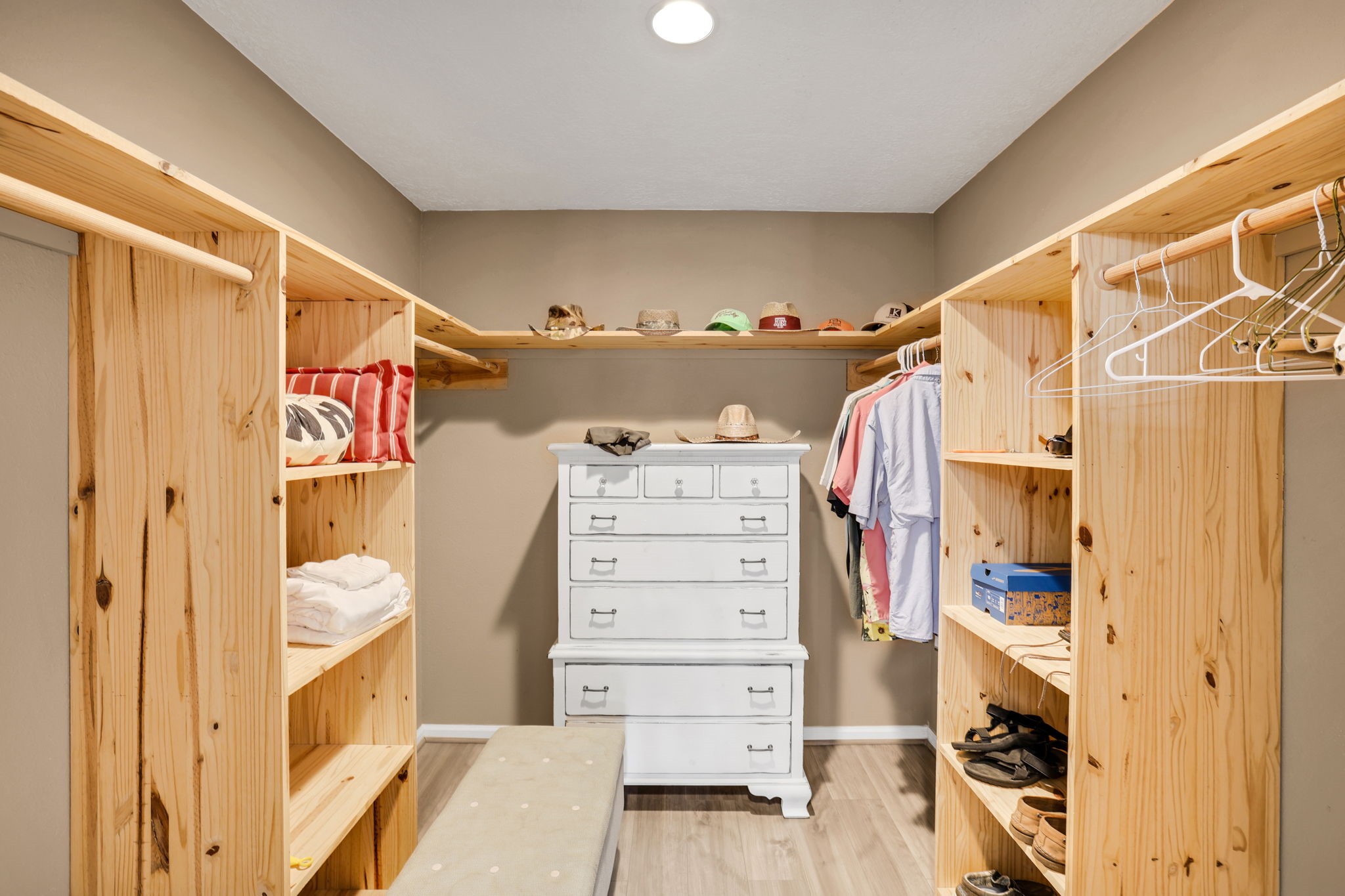 331 Holiday Lane Coldspring, TX 77331 - Photo 35 of 36 This photo shows a spacious walk-in closet with natural wood shelving and hanging space. It features a white dresser, ample storage for clothes and accessories, and a bench for convenience.