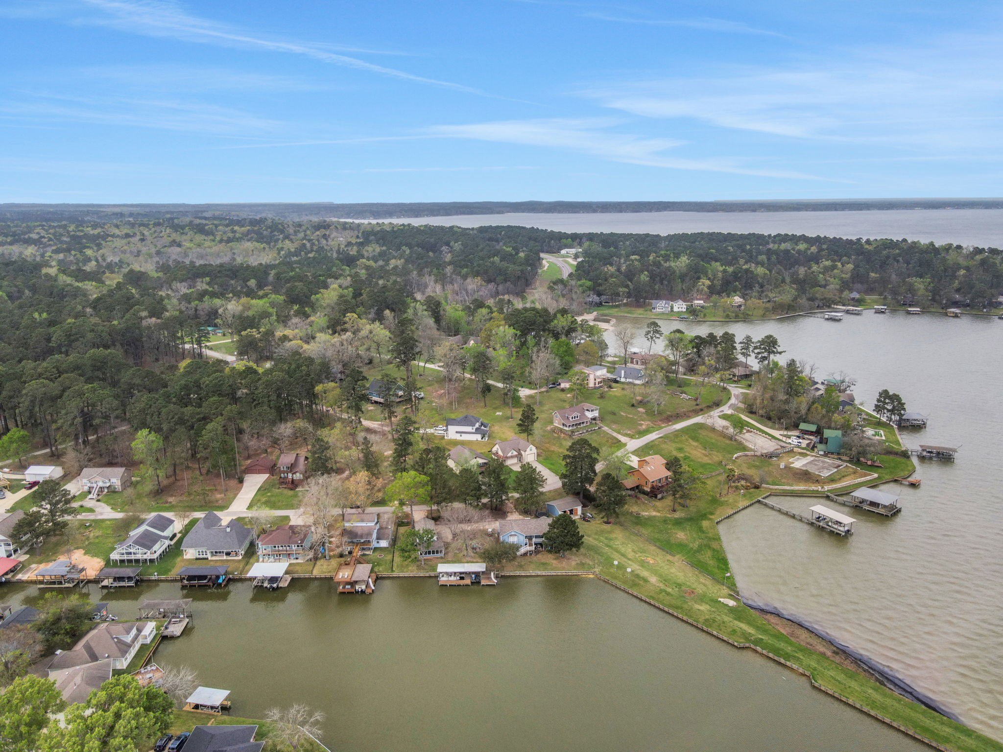 331 Holiday Lane Coldspring, TX 77331 - Photo 5 of 36 This aerial photo showcases a serene lakeside neighborhood with tree-lined streets and a variety of homes, some with private docks. The area is surrounded by lush greenery and offers picturesque water views, ideal for those seeking a peaceful, nature-oriented lifestyle.