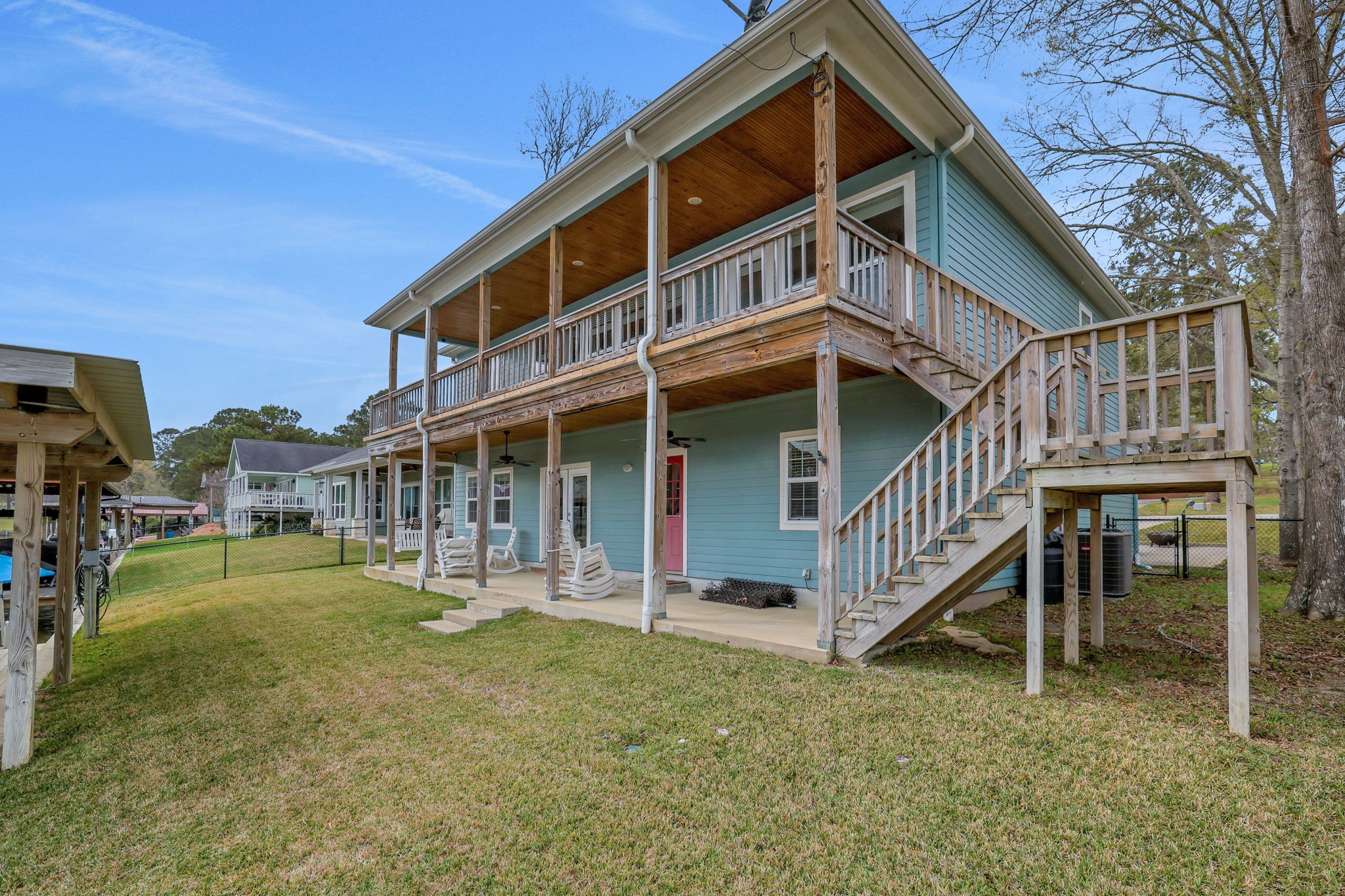 331 Holiday Lane Coldspring, TX 77331 - Photo 6 of 36 The back of the home features a spacious wooden balcony, ideal for relaxing outdoors. Recently added stairs from the balcony to the back patio for convenience. The property includes a well-maintained lawn and a surrounding fence for added privacy.